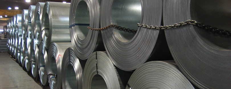 Large coils of galvanized steel sheet metal stored in an industrial warehouse for manufacturing and construction use
